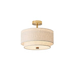 Clérachic ceiling light in gold and linen, with a round brass canopy, a short stem and a lit white diffuser underneath, on white.