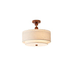 Clérachic walnut and linen light with a two-ball wooden stem, lit softly under its stacked linen shades on a white backdrop.