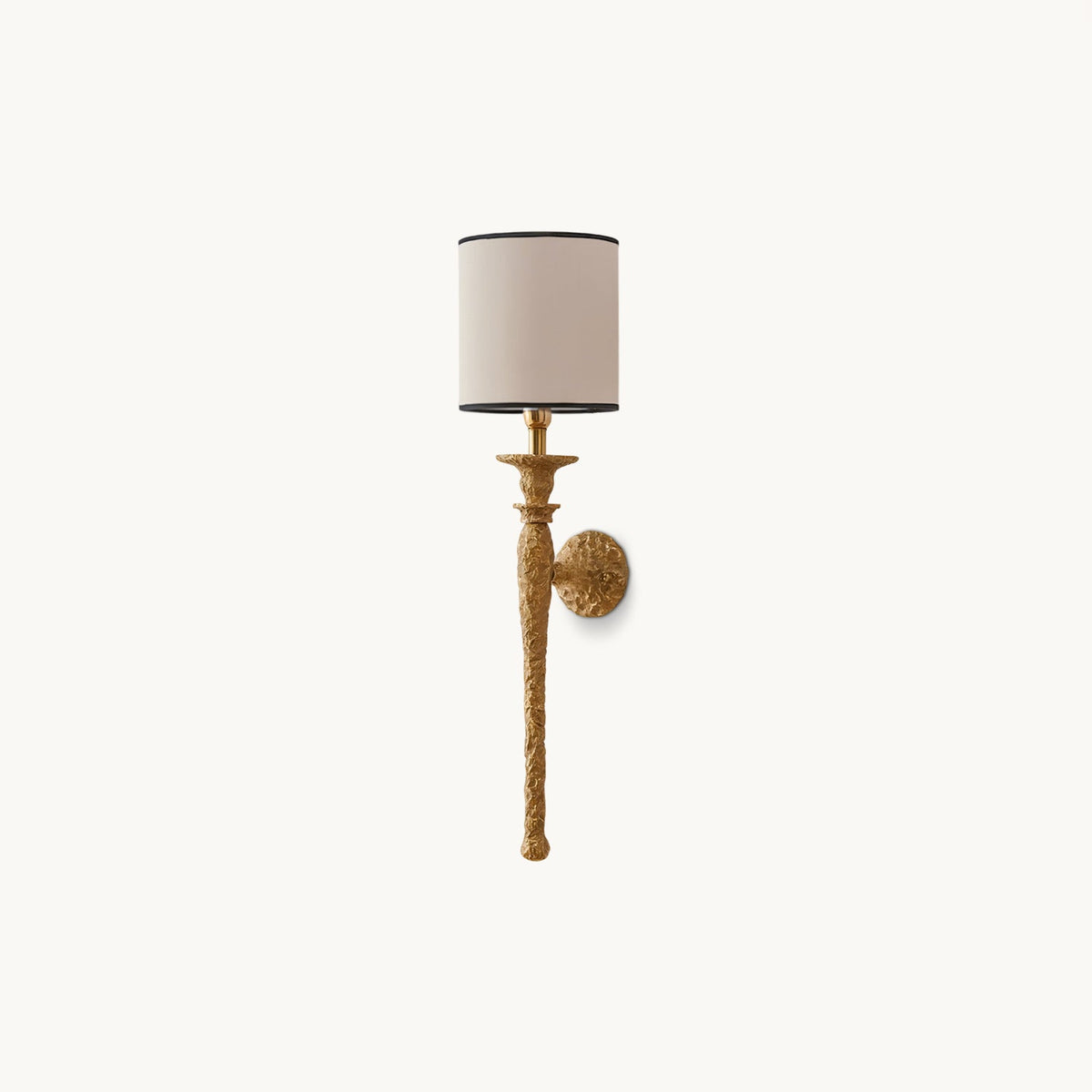 Clérachic wall light with a slim beige cylinder shade on a textured antique brass stem and round wall plate, unlit on a plain white backdrop.