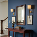 Two Clérachic brass wall lights frame a dark-wood mirror on a navy wall, above a hall console and near a staircase.