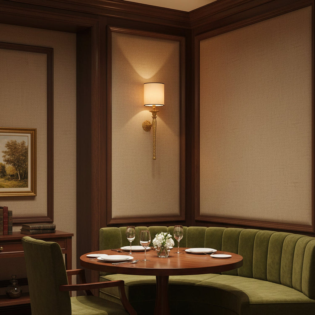 A Clérachic brass wall light lights a panelled dining nook with a round table and a green curved banquette.