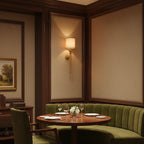 A Clérachic brass wall light lights a panelled dining nook with a round table and a green curved banquette.