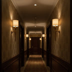 Clérachic wall lights line both sides of a long, dim hallway with patterned walls, their shades glowing warm.