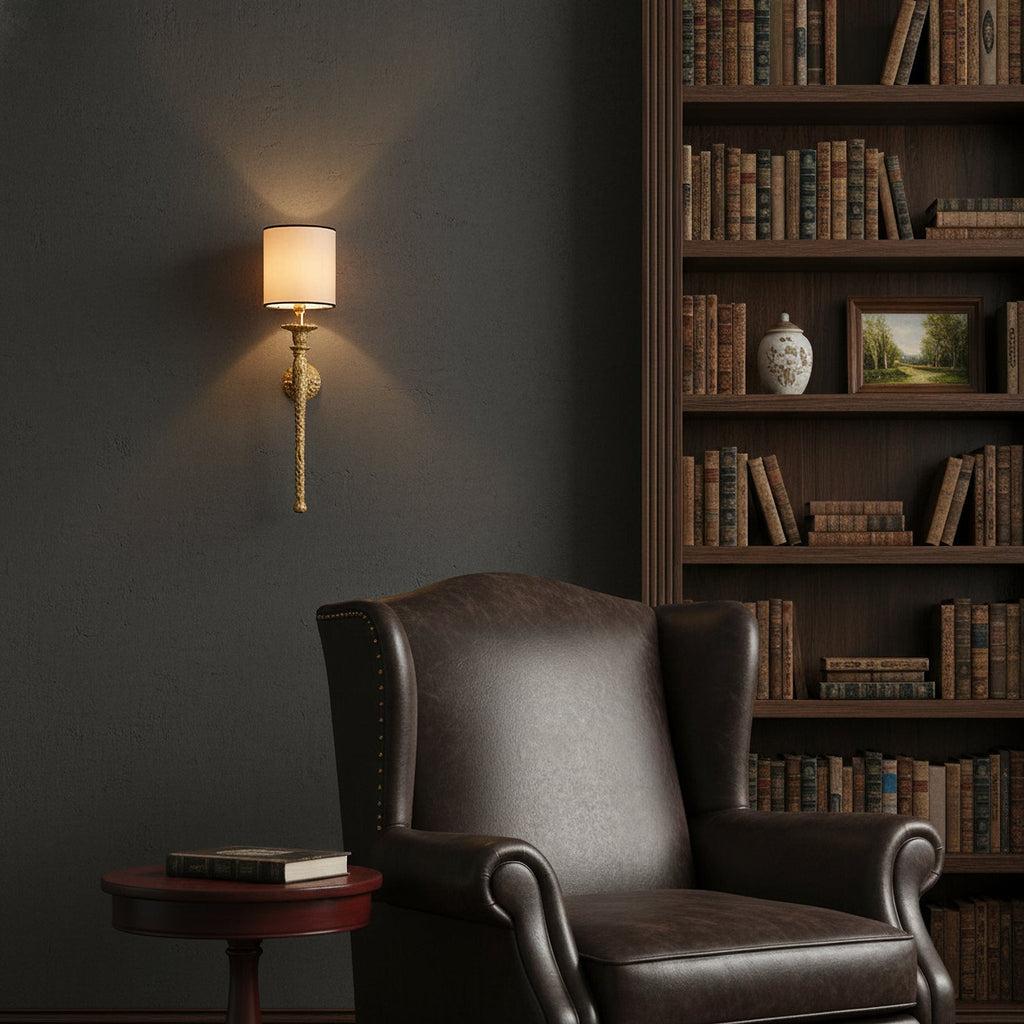 Small Clérachic brass wall light above a dark leather armchair, with a bookcase of old books and a dark grey wall behind.