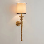 The lit beige shade and hammered antique brass stem of this Clérachic wall light on a pale wall, with light washing up and down.