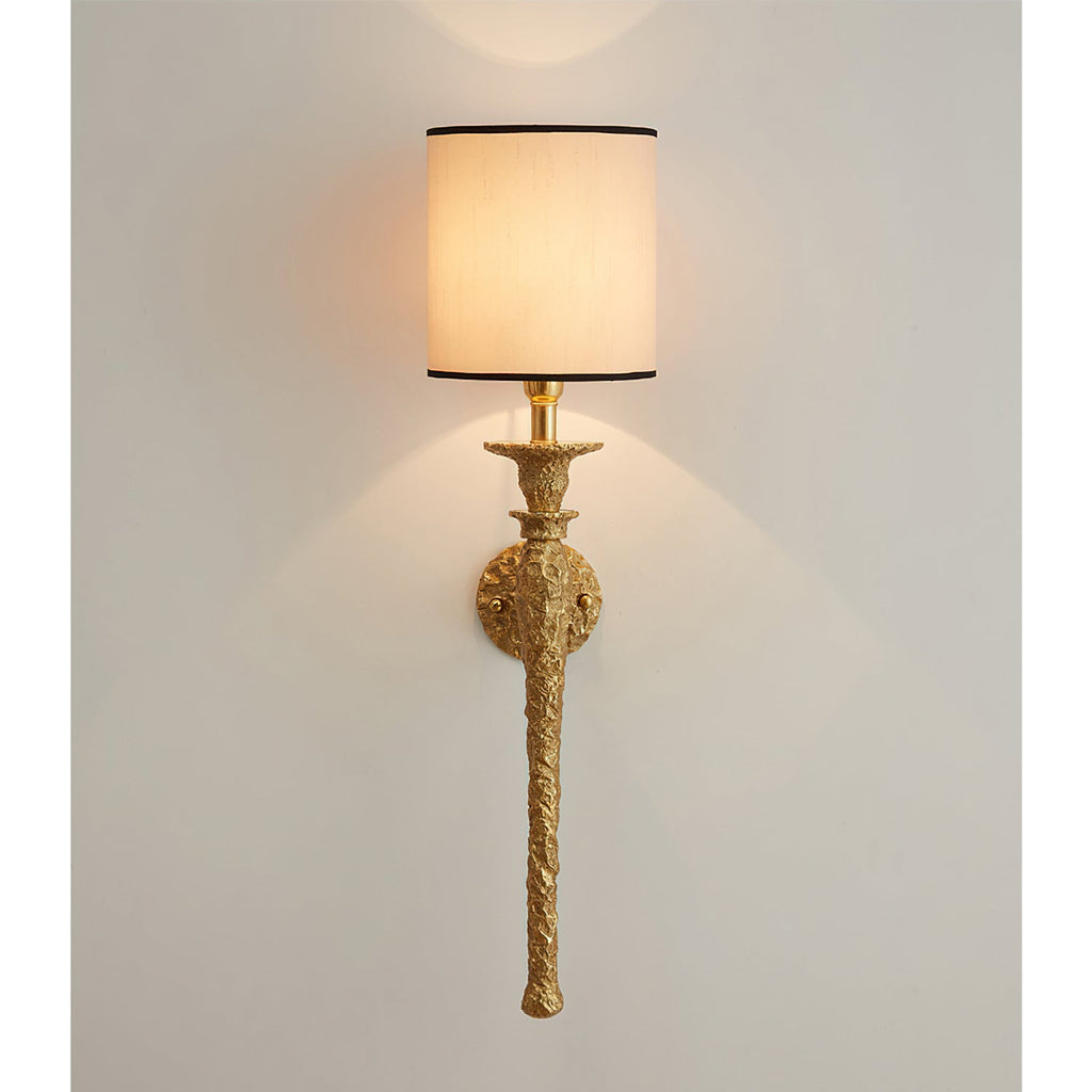 Beige shade with a black trim on this Clérachic wall light, lit and casting soft arcs of light up and down a grey-white wall.