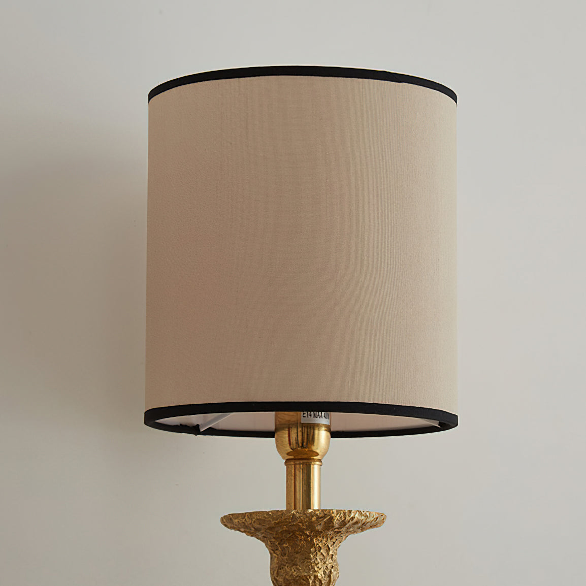 Close view of the beige fabric shade with black piping on this Clérachic wall light, above the brass lamp holder.
