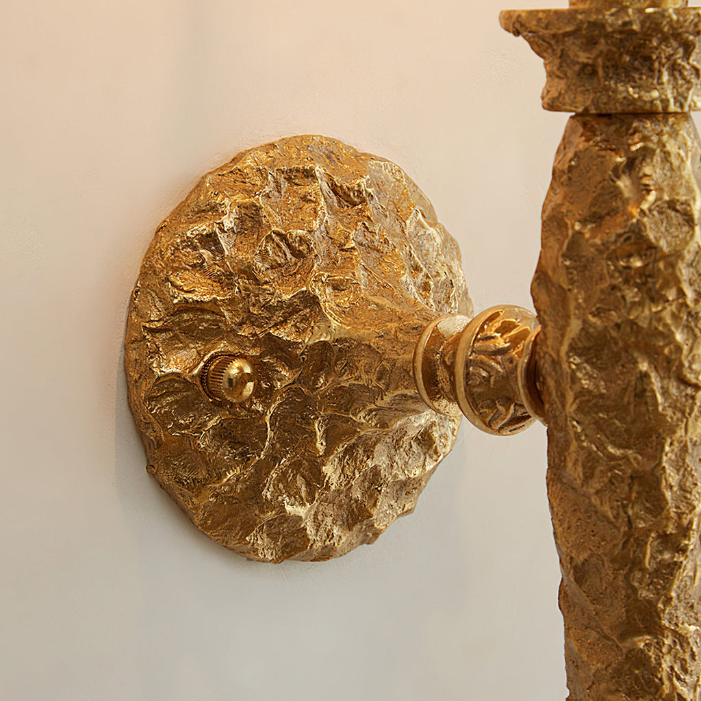 Close view of the round, rough-textured brass wall plate and arm joint on this Clérachic wall light.