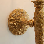 Close view of the round, rough-textured brass wall plate and arm joint on this Clérachic wall light.