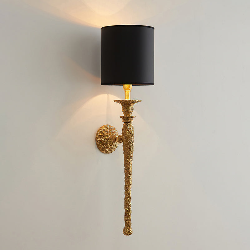 Black-shaded Clérachic wall light with an antique brass stem, lit on a pale wall and seen from a distance.
