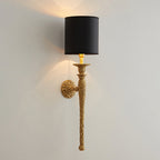 Black-shaded Clérachic wall light with an antique brass stem, lit on a pale wall and seen from a distance.
