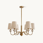 Clérachic chandelier with six tapered linen shades, white ceramic necks and curved gold arms on a central rod, on a plain white backdrop.