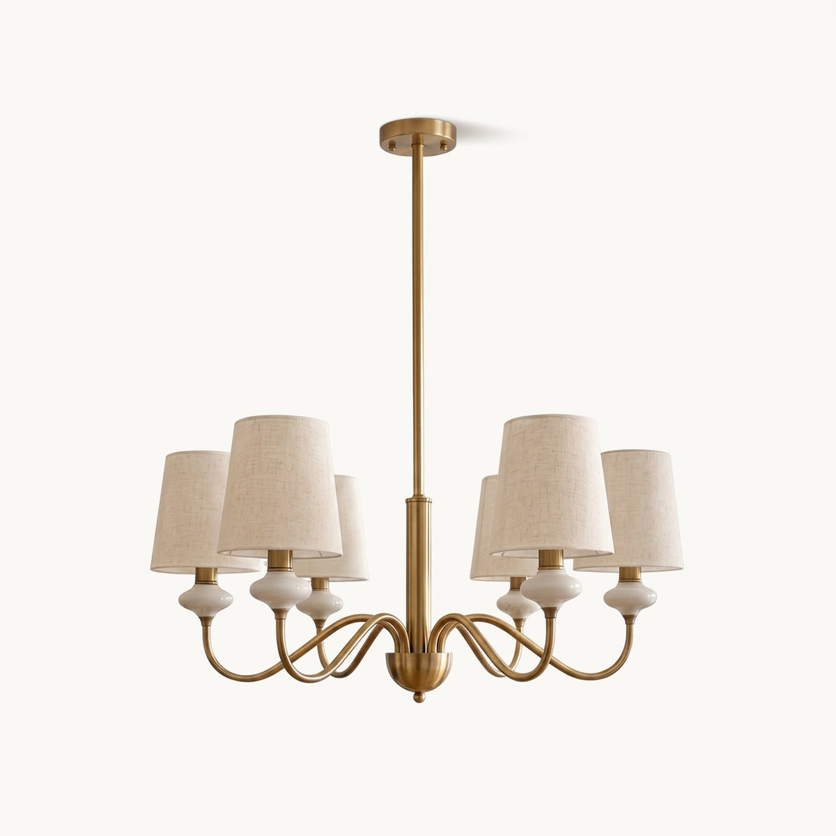 Clérachic chandelier with six tapered linen shades, white ceramic necks and curved gold arms on a central rod, on a plain white backdrop.