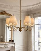 A gold six-light Clérachic chandelier hangs from a long rod in a Parisian room with a gilt mirror, cornicing and tall windows.