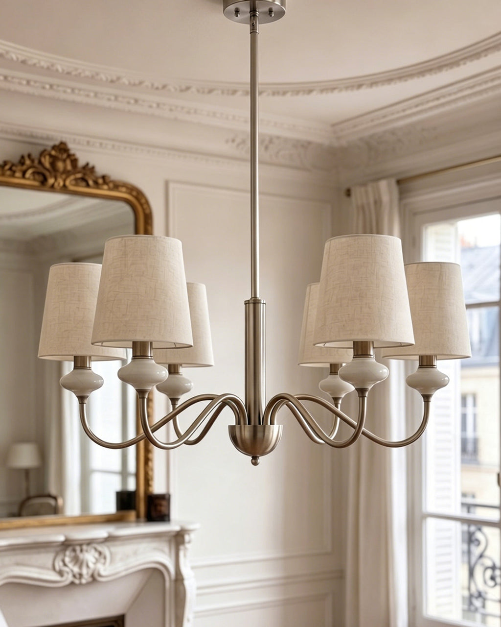 The sand nickel version of this Clérachic chandelier hangs in a cornice-ringed room, its linen shades beside a gilt-framed mirror.