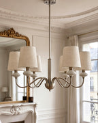 The sand nickel version of this Clérachic chandelier hangs in a cornice-ringed room, its linen shades beside a gilt-framed mirror.