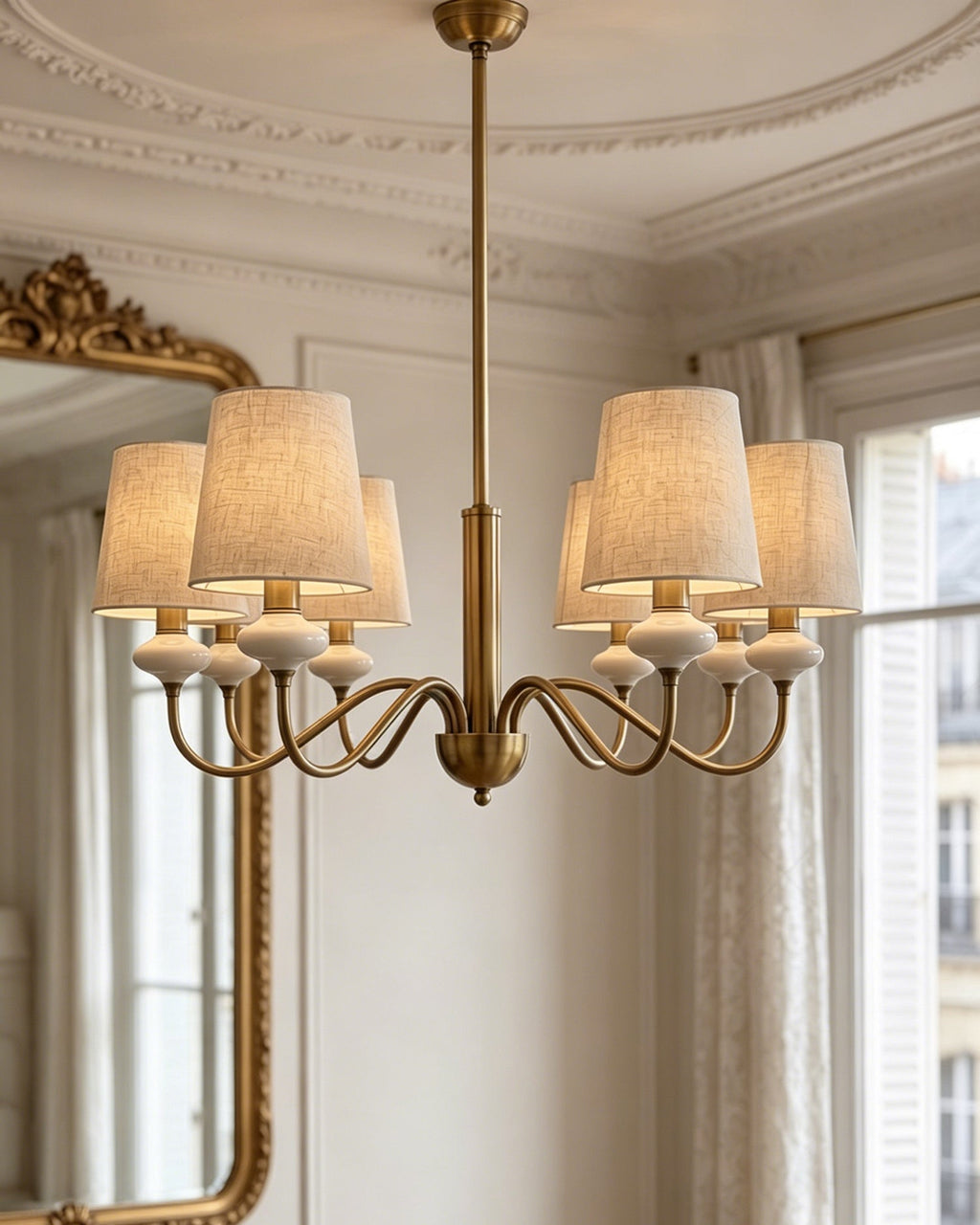 Gold Clérachic chandelier seen from slightly below, with six linen shades and looped arms against a white panelled wall.