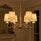 Lit at dusk, the linen shades of this Clérachic chandelier glow warm gold in a darkened room with a mirror and tall windows.