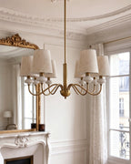 Wide view of a gold Clérachic chandelier hanging in the middle of a high-ceilinged room, with a fireplace and mirror at the side.