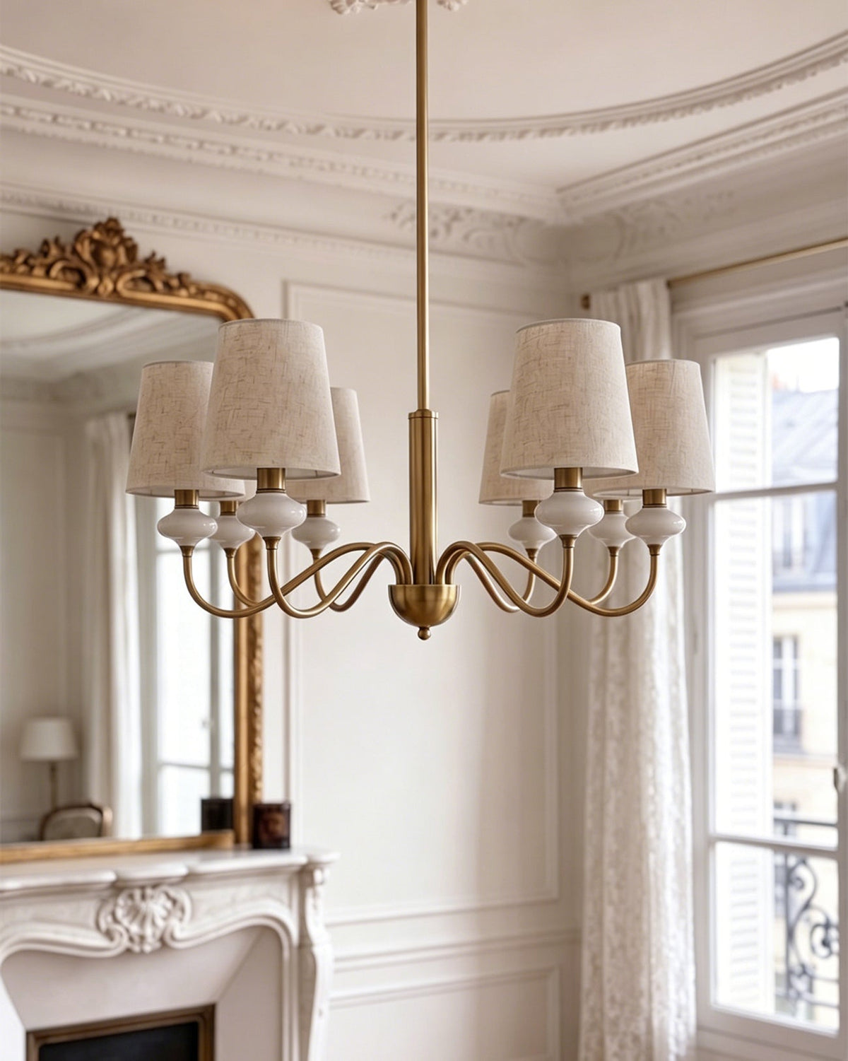 Wide view of a gold Clérachic chandelier hanging in the middle of a high-ceilinged room, with a fireplace and mirror at the side.
