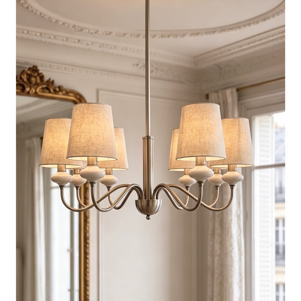 Sand nickel Clérachic chandelier with six linen shades, hung before a gilt mirror and shuttered windows.