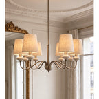 Sand nickel Clérachic chandelier with six linen shades, hung before a gilt mirror and shuttered windows.
