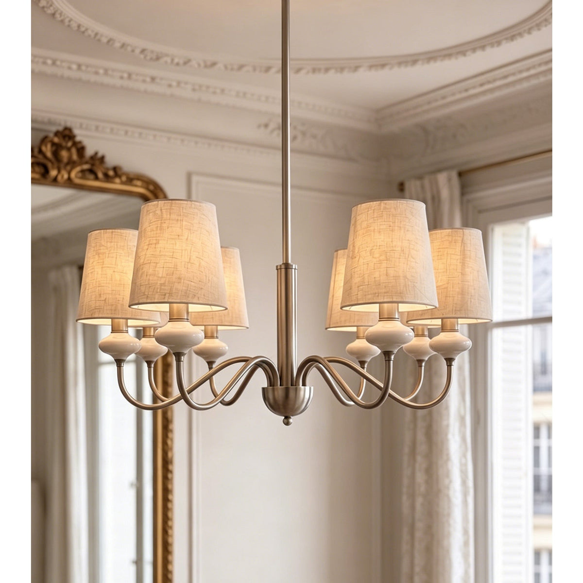 Sand nickel Clérachic chandelier with six linen shades, hung before a gilt mirror and shuttered windows.