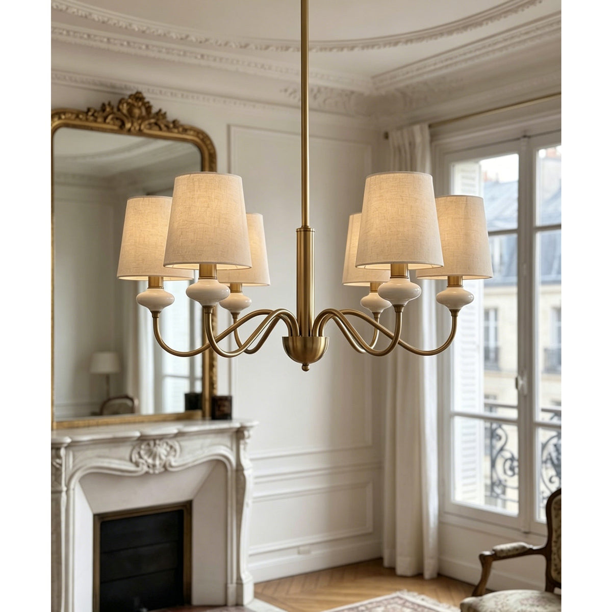 Six-light Clérachic chandelier in gold with linen shades, set against a mirror, a fireplace and a French window.