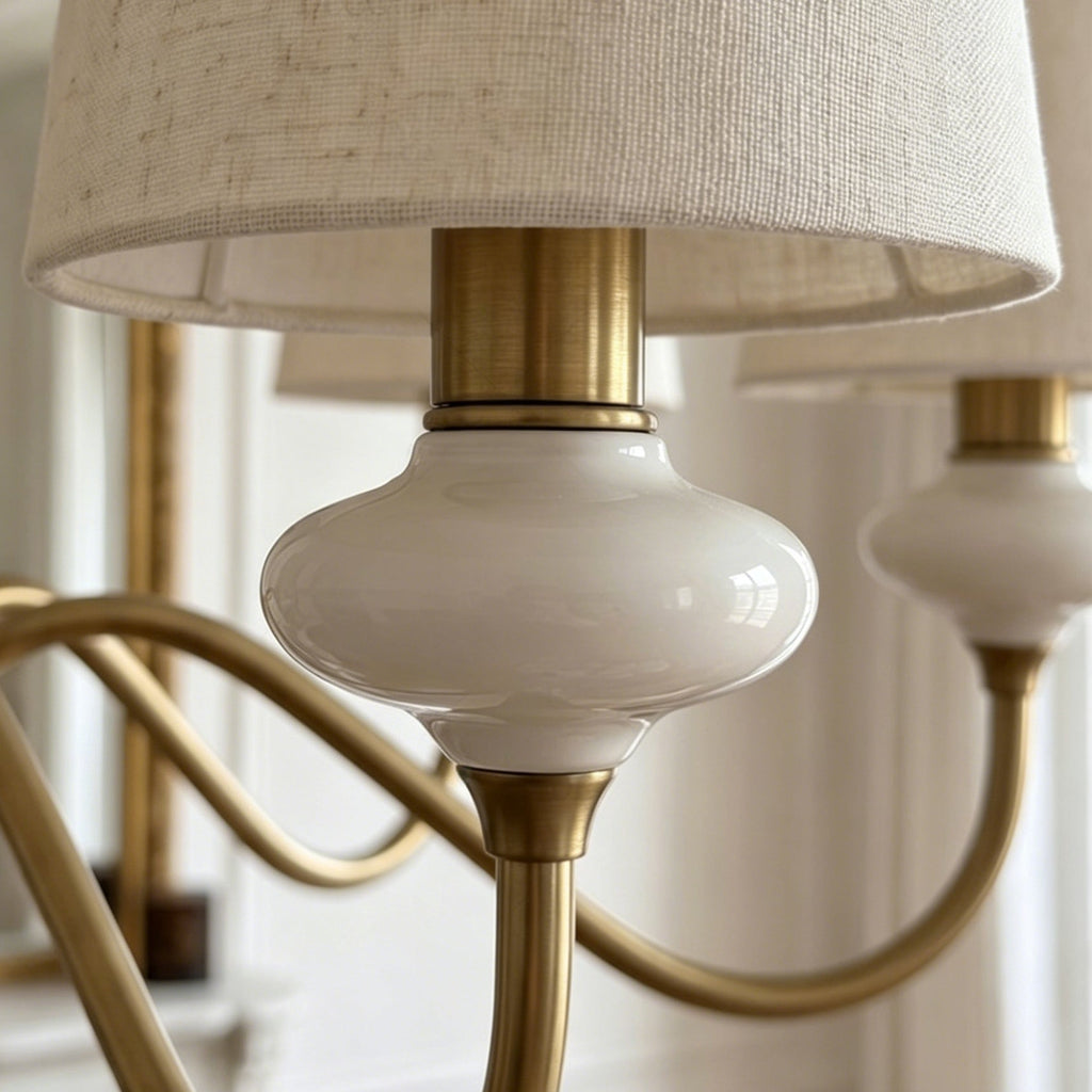 Close view of a glossy white ceramic neck, brass socket collar and curved gold arm on this Clérachic chandelier.