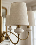 Close view of a textured linen shade above a cream ceramic neck on this Clérachic chandelier, with a gilt mirror blurred behind.
