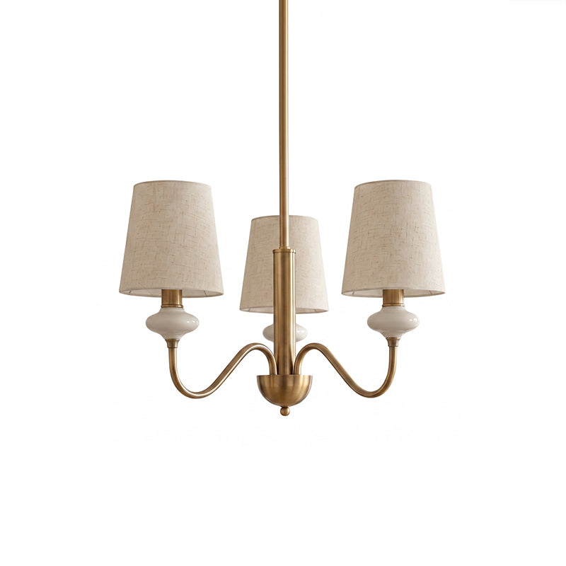 Gold three-light Clérachic chandelier with linen shades, ceramic necks and curved arms, on a plain white backdrop.