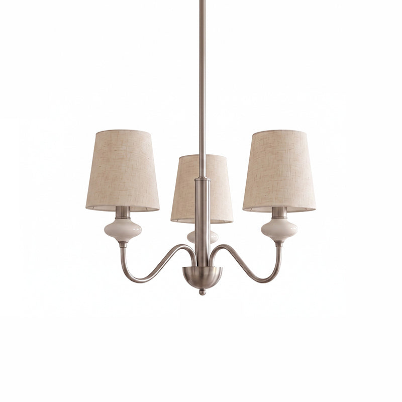 Three-light Clérachic chandelier in a sand nickel finish, with linen shades and ceramic necks, on a plain white backdrop.
