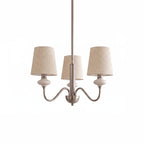 Three-light Clérachic chandelier in a sand nickel finish, with linen shades and ceramic necks, on a plain white backdrop.