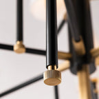 Close view of a fluted brass knob on the end of a black arm on this Clérachic chandelier, with a soft white shade out of focus behind.
