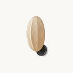 A Clérachic wall light on a plain white backdrop, an upright oval of woven linen with a centre ridge on a black round wall mount.