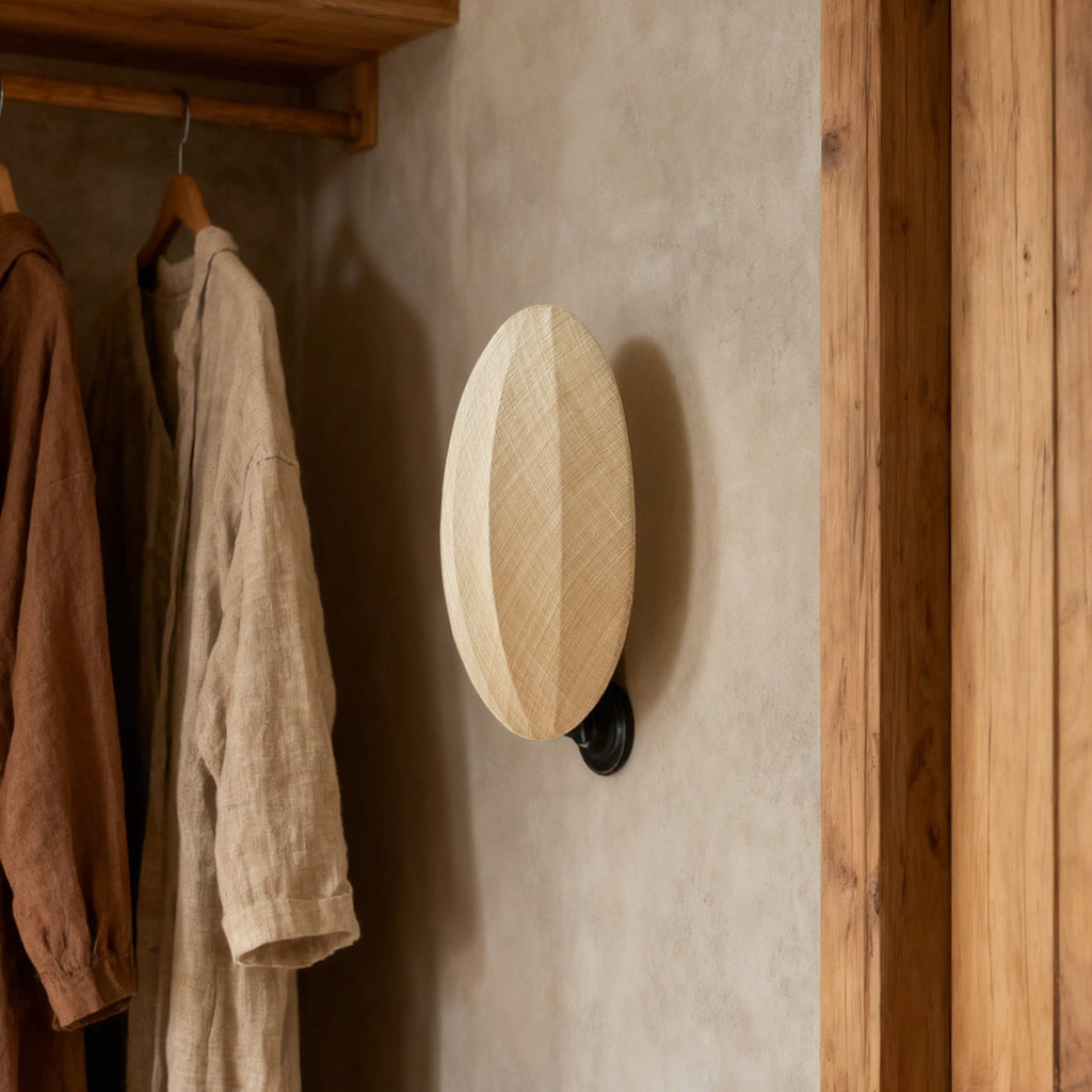 Against a plaster wall next to hanging linen shirts and a timber door frame, this Clérachic wall light shows its ribbed oval shade.