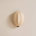 Close view of this Clérachic wall light on a plain cream wall, its rounded linen shade and its vertical ridge casting a soft shadow.