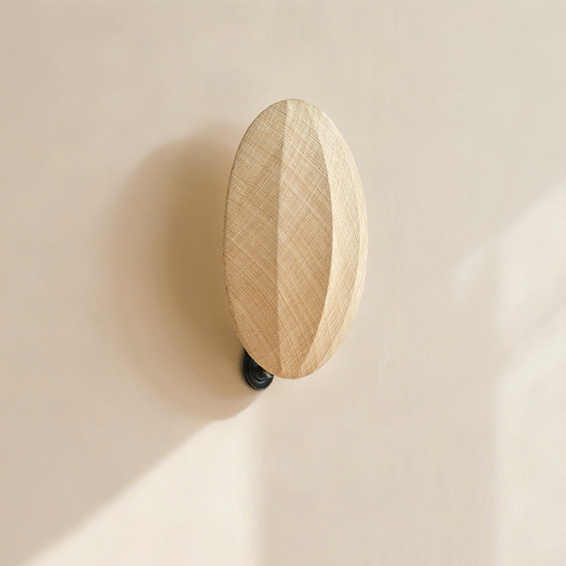 Seen from below on a sunlit wall, this Clérachic wall light shows its tall oval linen shade and small black mounting arm.