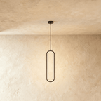 Clérachic slim black oval LED loop pendant, its inner edge glowing warm, hung from a cord on a limewashed wall.