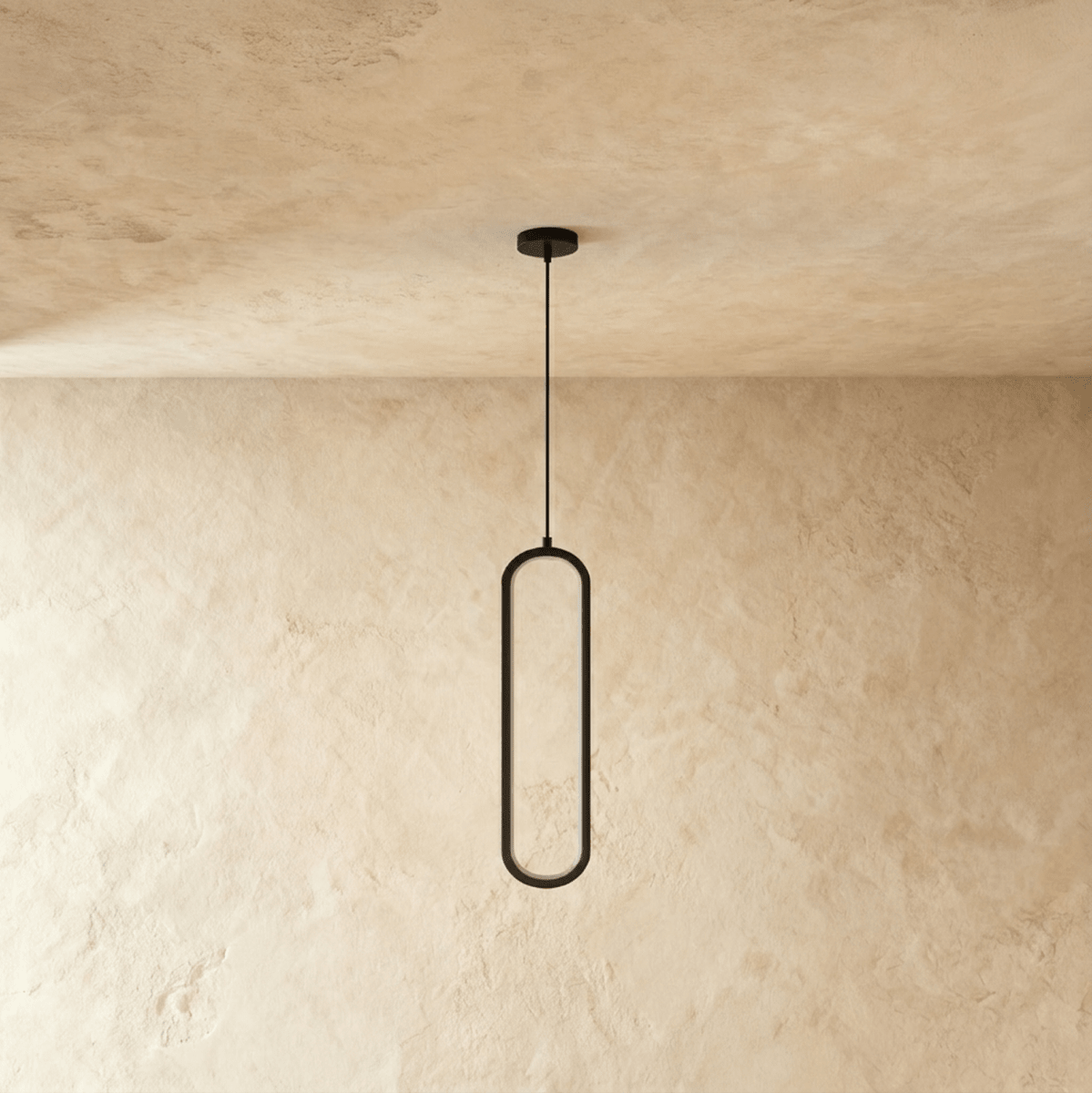 Clérachic slim black oval loop pendant, unlit, hung from a black cord and round canopy against a plaster wall.