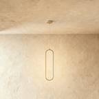Clérachic slender brushed gold oval LED loop pendant glowing softly on a thin cord against a warm plaster wall.