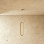 Clérachic slender brushed gold oval loop pendant, switched off, on a clear cord and gold canopy against plaster.