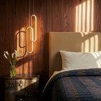 Clérachic double gold oval loop pendant glowing over a bedside in a walnut-panelled bedroom with a cream headboard.