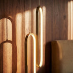 Close view of two interlocked Clérachic brushed gold oval rings with a soft LED glow against walnut panelling.