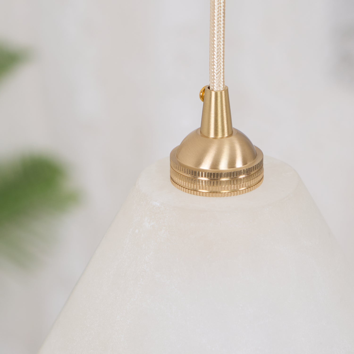 The Clérachic brass collar in close-up where it meets the alabaster cone, soft greenery blurred behind.