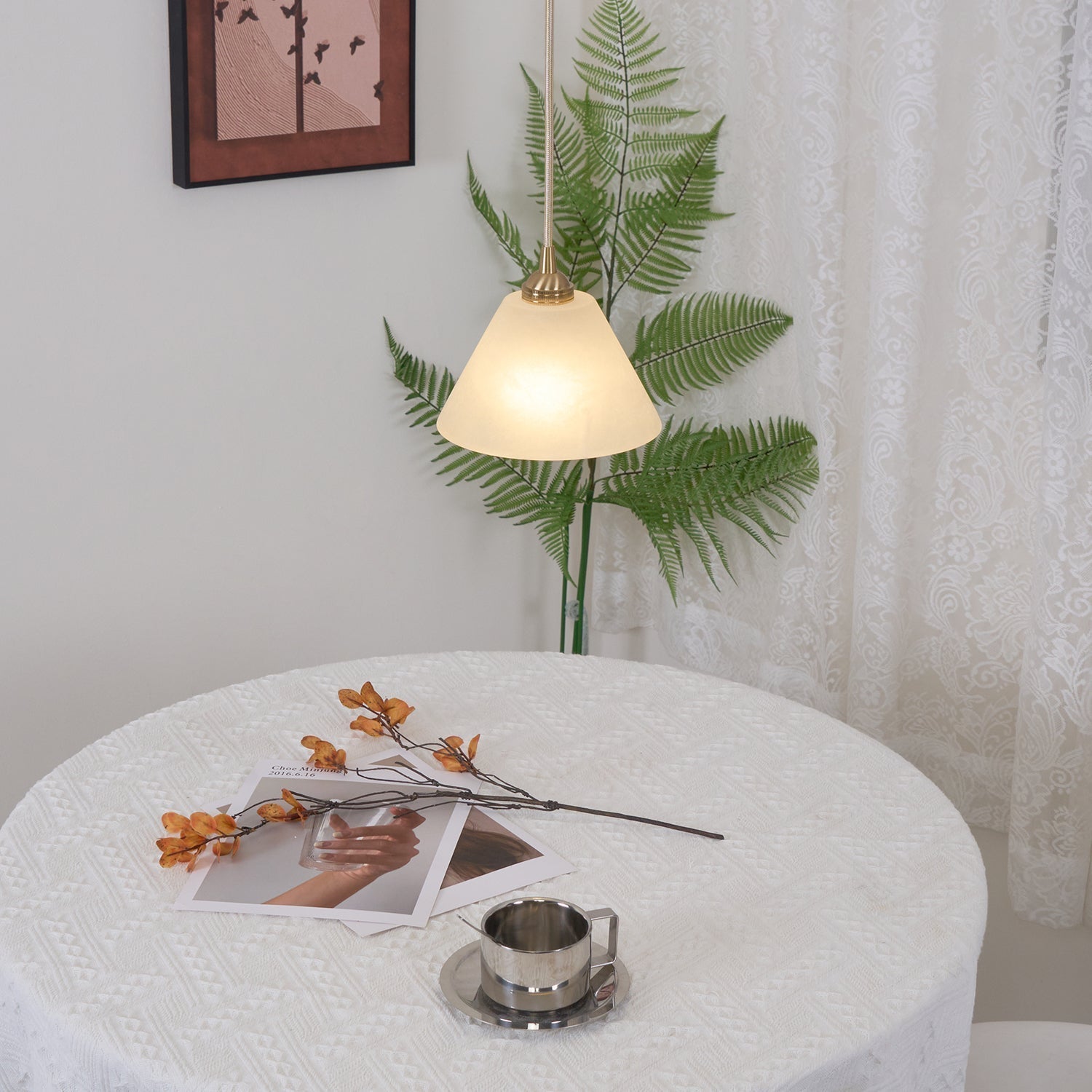 The Clérachic light lit above a round lace-covered table with a fern and framed print in a bright corner.