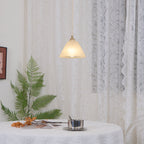 The Clérachic cone hung low over a styled tabletop, its shade warm against pale lace drapery.