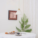 The Clérachic light seen from an angle beside a small framed print, fern leaves brushing the wall below.