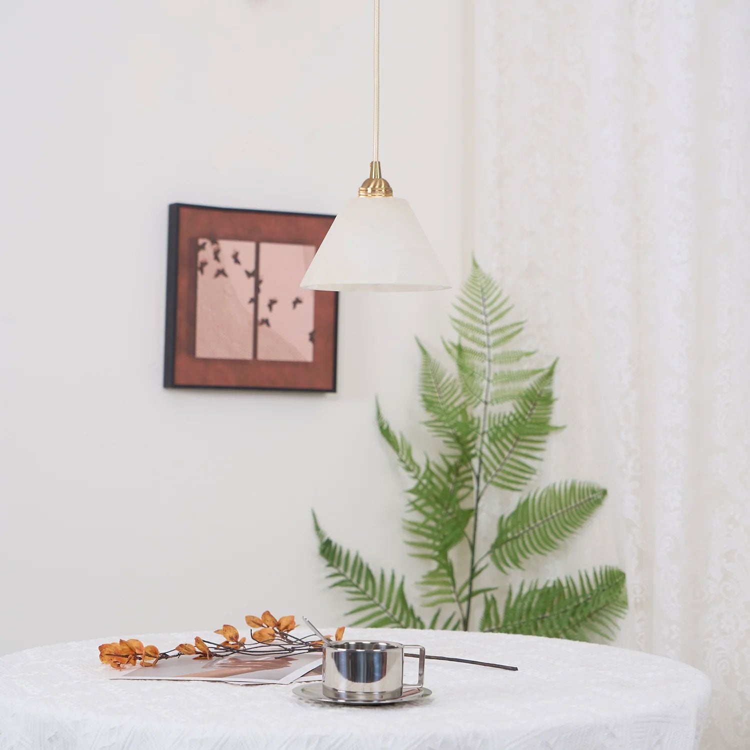 The Clérachic light seen from an angle beside a small framed print, fern leaves brushing the wall below.