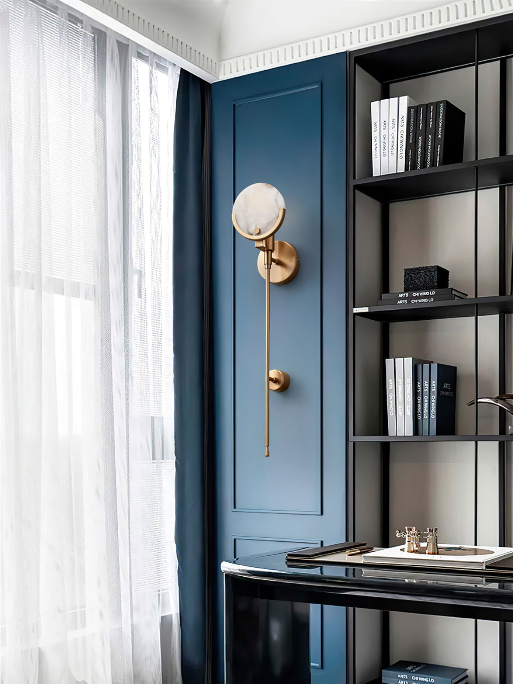 Clérachic wall sconce mounted on deep blue joinery beside a study window, its alabaster disc catching the daylight.